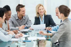 A team of employees smiling during a workplace meeting, representing how micro-market vending installations improve morale and employee engagement.