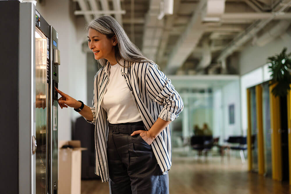 Woman selecting a snack from a vending machine inside a modern office